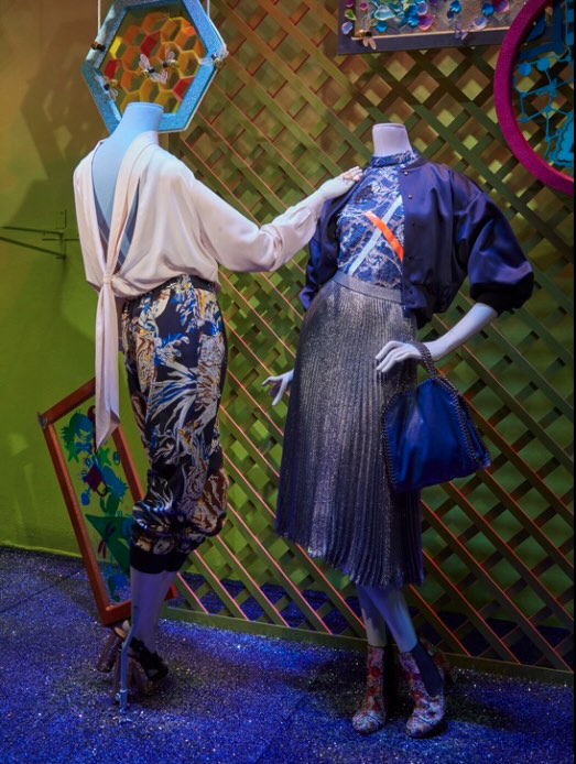 Two mannequins dressed in fashionable clothes in front of multi-coloured trellis
